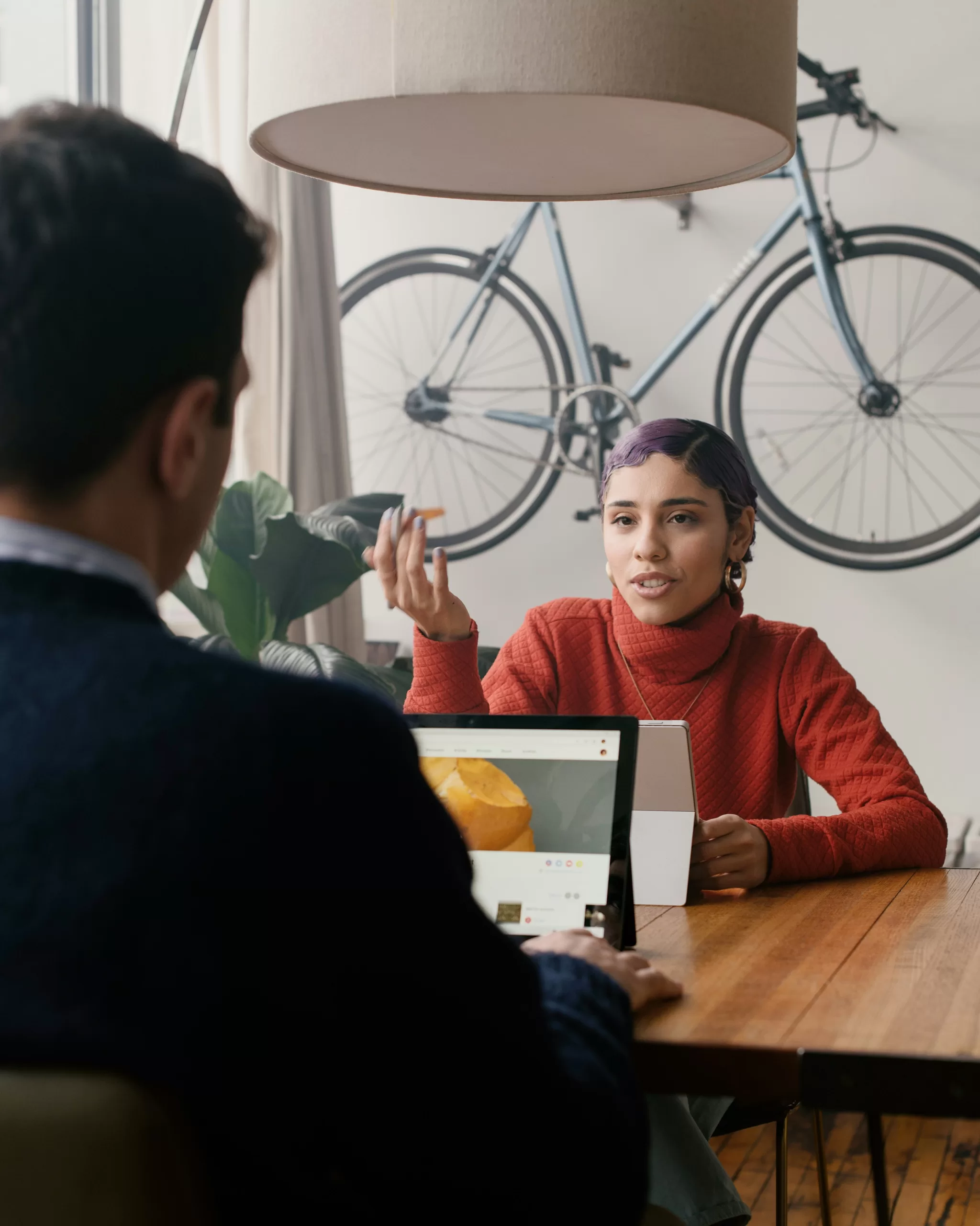Eine Frau spricht mit einem Mann an einem Tisch sitzend. Ein Fahrrad hängt an der Wand